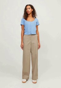 Light blue, ribbed short-sleeve top with button closure, paired with high-waisted beige wide-leg trousers and white sneakers with beige accents.