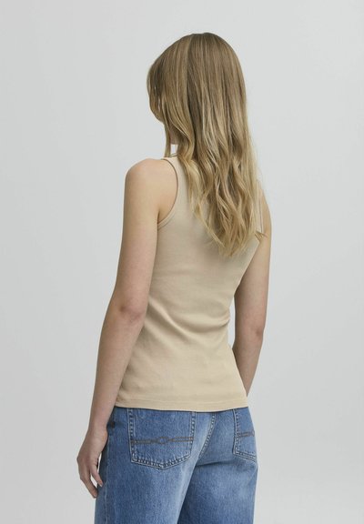 Top de tirantes beige con textura acanalada, diseño ajustado y tirantes finos, combinado con unos vaqueros de mezclilla de cintura alta de color azul claro.