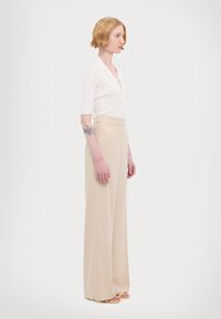 Top bianco a maniche corte con effetto costina e dettagli con lacci, abbinato a pantaloni beige a gamba larga, caratterizzati da una trama liscia e un design a vita alta.