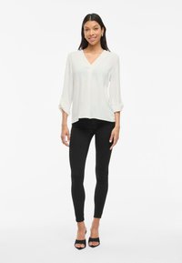 Hvid v-hals bluse, lange ærmer oprullet, parret med sorte skinny jeans og sorte åbne hæle. Glat tekstur, afslappet pasform.