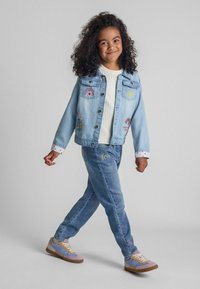 Denim striukė su spalvingais siuvinėjimais: vaivorykštės ir saulės, derinama su šviesiai mėlynomis džinsinėmis kelnėmis, taip pat su panašiais puošybos elementais. Violetiniai sportbačiai užbaigia įvaizdį.