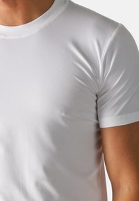 T-shirt bianco in cotone a maniche corte con scollo rotondo e texture liscia, caratterizzato da un design aderente che mette in evidenza la parte superiore del corpo.