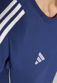Navy blue athletic shirt with white three-stripe detail on shoulders and a white logo. Soft fabric, crew neck, and fitted design.