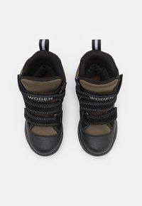 Zapatos de caña alta en negro y verde oliva con parte superior de malla texturizada, asegurados por dos correas de velcro negras, presentando una puntera reforzada.