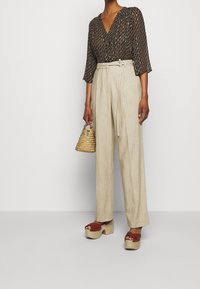 Blus med blommönster och V-ringning, kombinerad med beige vida byxor, röda platåsandaler och en liten vävd handväska.
