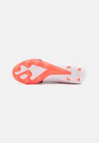 Scarpa da calcio con una tomaia bianca, accenti neri e una suola corallo vivace dotata di tacchetti conici per una maggiore trazione su superfici erbose.