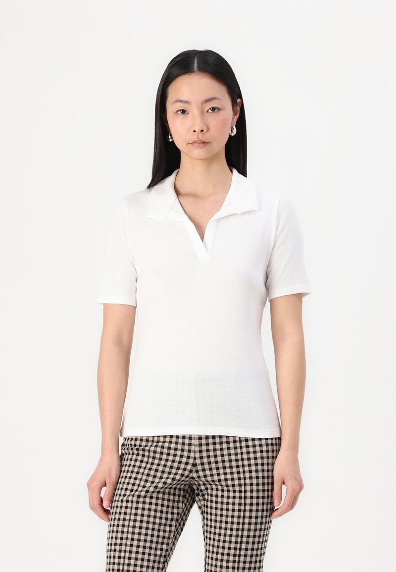 Hvid polo shirt med korte ærmer, med en sammenfoldet krave og en slim fit. Struktureret stof kombineret med ternede bukser i sort og beige.