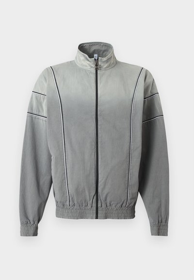 Ανοιχτό γκρι μπουφάν με φερμουάρ και ψηλό γιακά, ελαστικά μανσέτες και κάτω μέρος, με κάθετες και οριζόντιες μαύρες λεπτομέρειες σε γραμμή στο μπροστινό μέρος και τα μανίκια.