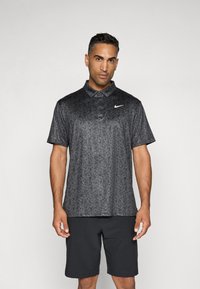 Černé polo tričko s texturovaným květinovým vzorem, krátkými rukávy a límečkem. Na levé horní části hrudi je bílé logo Nike.