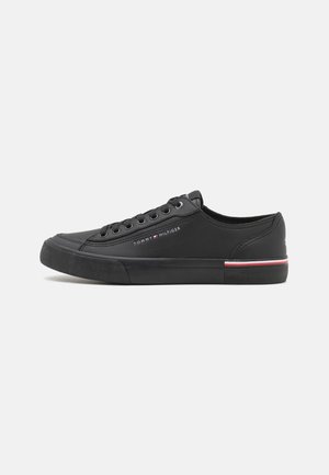 Basket basse noire avec lacets noirs, semelle en caoutchouc, détail à rayures rouges et blanches, et logo Tommy Hilfiger sur le côté.