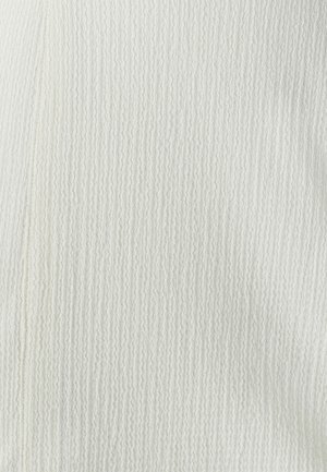 Biely textúrovaný materiál s rebrovaným vzorom, na ktorom sú jemné línie prebiehajúce vertikálne. Povrch sa zdá byť jemný a mierne vyvýšený.