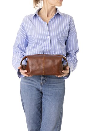 Borsa rettangolare in pelle marrone con zip superiore, manici laterali e dettagli di cucitura visibili, tenuta da una persona in una camicia a righe blu.