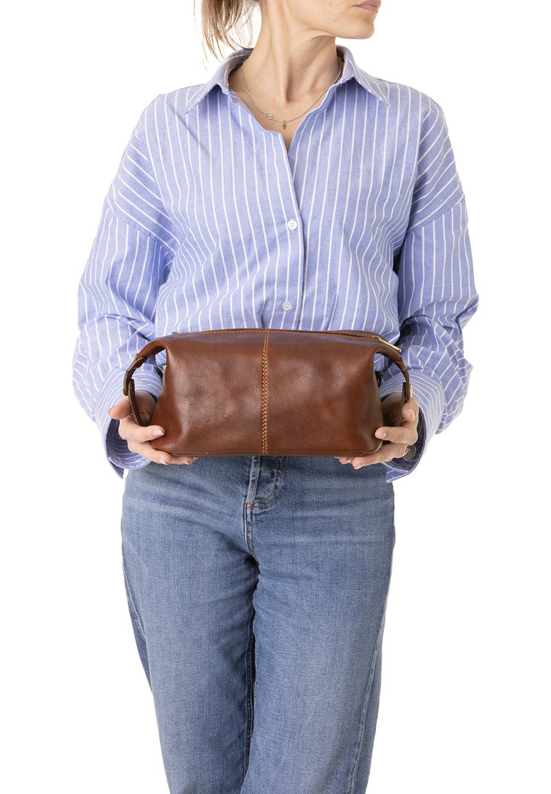 Borsa rettangolare in pelle marrone con zip superiore, manici laterali e dettagli di cucitura visibili, tenuta da una persona in una camicia a righe blu.