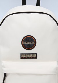 Zaino bianco con dettagli neri, dotato di una toppa rotonda con logo e un'etichetta rettangolare del marchio. Materiale liscio, compartimento principale con cerniera.