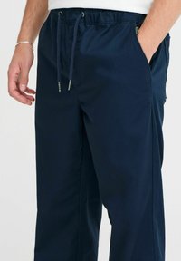 Marineblauwe sportbroek van gladde stof, met een elastische tailleband met trekkoorden, zijzakken en een ontspannen pasvorm.