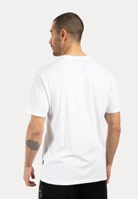 Camiseta blanca de algodón con mangas cortas, escote redondo y textura suave. Presenta una pequeña etiqueta en el dobladillo.