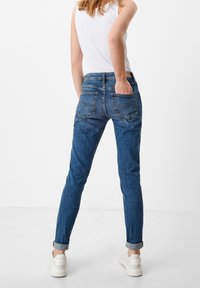 Slim-fit, blue denim jeans with rolled cuffs, five-pocket design, and tonal stitching. Worn with a white tank top and white sneakers.