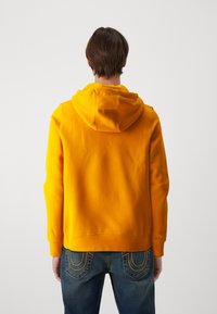 Mikina s kapucňou v jasne žltej farbe z fleece s rebrovanými manžetami, s stredne dlhým strihom a klokanou vreckom vpredu.