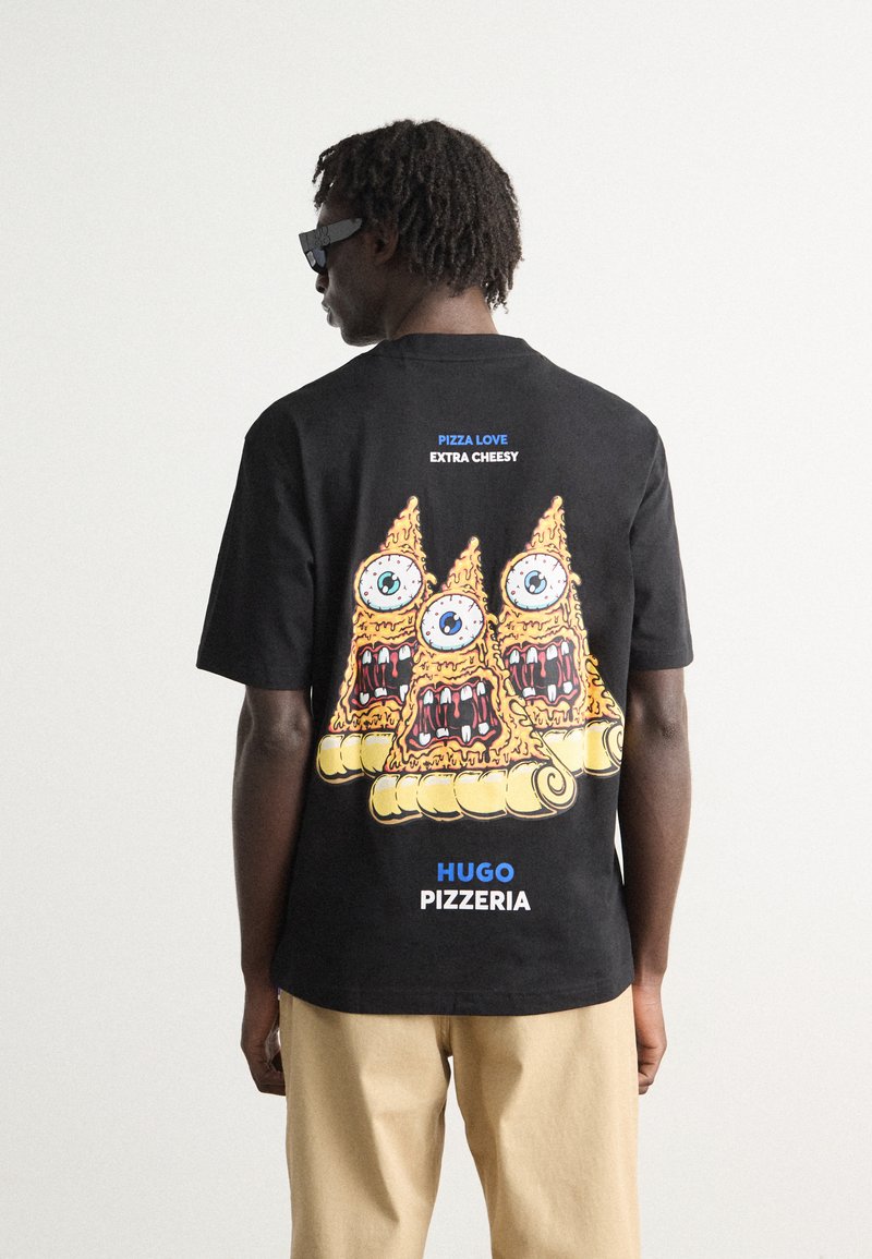 Svart t-skjorte med et fargerikt grafisk design av tre pizzastykker med øyne og munn. Teksten lyder "PIZZA KJÆRLIGHET EKSTRA OSTETE" og "HUGO PIZZERIA."