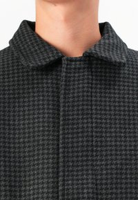 Manteau à motif pied-de-poule gris avec un col, réalisé en tissu texturé imitation laine et doté d'un plastron avant dissimulé.