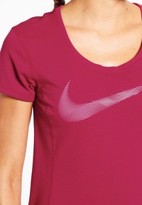 Kvinna som bär en röd kortärmad träningsskjorta med en vit randig Nike-swoosh-logotyp på bröstet.