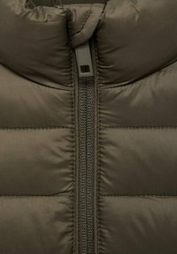 Olivgrön pufferjacka med hög krage, kviltad textur och en central dragkedja med en tygdragare för stängning.