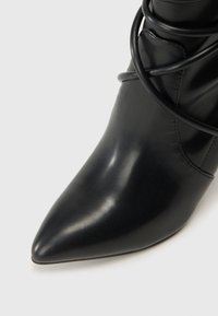 Čierne kožené členkové čižmy s ostrou špičkou a šnúrkami obtočenými okolo hornej časti na neutrálnej pozadí.