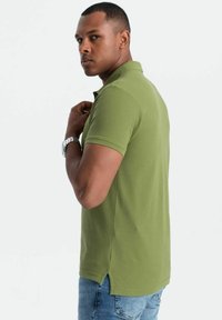 Grøn polo skjorte lavet af bomuld, med klassisk krave, korte ærmer og sideslids, parret med blå denim jeans.