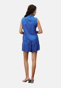 Blauwe mouwloze top van textuurstof, gecombineerd met bijpassende shorts. Heeft een losse pasvorm en wordt aangevuld met grijze blokhak sandalen.