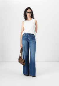 Top branco sem mangas, jeans de perna larga azuis, sapatos pretos, bolsa castanha e óculos de sol escuros. Tecido suave, corte descontraído e estilo casual.