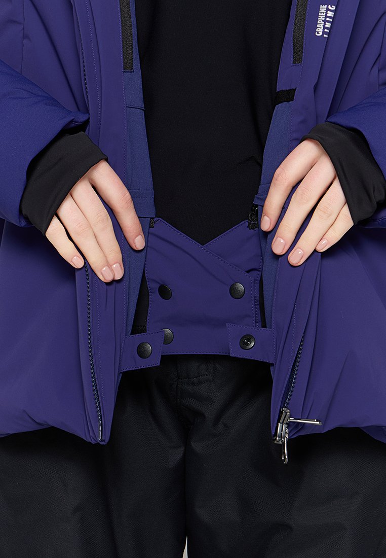 Giacca da esterno viola con fodera interna nera e chiusure a scatto. Cerniere visibili e maniche strutturate. Mani posizionate vicino all'apertura.