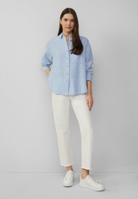 Blauw-wit gestreepte blouse met lange mouwen, gecombineerd met witte cropped broeken en witte sneakers. Soepele stoftextuur.