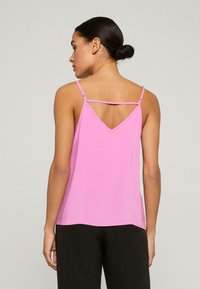 Roze mouwloos topje met een V-achterkant, gemaakt van gladde stof. Beschikt over verstelbare bandjes en een relaxte pasvorm, perfect voor het combineren met andere kleding.