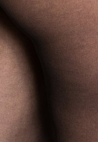 Collant opachi marroni con texture a coste, mostrati dalla coscia verso il basso, caratterizzati da una cucitura liscia e quasi invisibile.