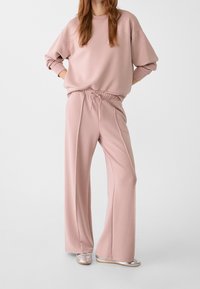 Helle rosa Sweatshirt mit leicht fallenden Schultern, kombiniert mit passenden weit geschnittenen Hosen mit elastischem Bund und Kordelzug. Silberne Schuhe.