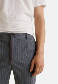 Pantalones grises a rayas con cierre de cordón, con una textura suave y bolsillos laterales, combinados con una camisa blanca de manga corta.