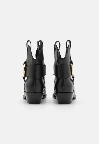 Botine din piele neagră cu vârf rotund, toc jos și un accent decorativ din aur pe lateral. Dispun de mânere pentru o încălțare ușoară.