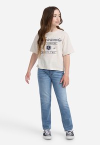 Svijetlosmeđi kratki majica s mornarskim grafičkim otiskom, uparen s svijetloplavim trapericama i crnim niskim tenisicama.