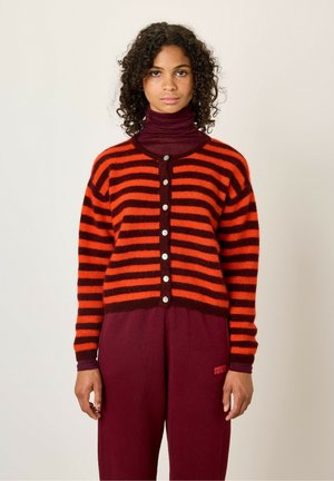 Cardigan a righe rosse e nere con scollatura tonda, chiusura a bottoni, texture pelosa e maniche lunghe, indossato sopra un dolcevita viola.