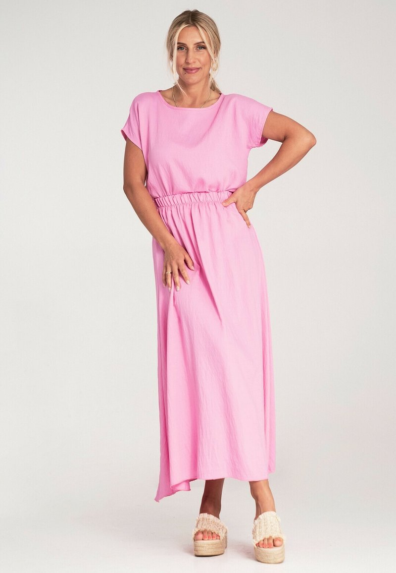 Różowa maxi sukienka z krótkimi rękawami i elastycznym pasem, charakteryzująca się zwiewnym krojem i gładką fakturą, w połączeniu z platformowymi sandałami.