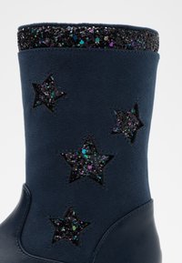 Stivale in suede blu navy con bordi a motivo stellato nero glitterato, caratterizzato da forme a stella ritagliate accentuate con paillettes multicolori.