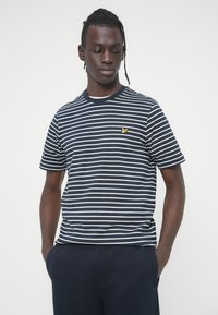 Μπλούζα με κοντό μανίκι σε μπλε ναυτικό και άσπρη ριγέ, με στρογγυλή λαιμόκοψη και μικρό κίτρινο έμβλημα στο στήθος. Μαλακό βαμβακερό ύφασμα.