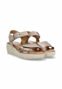 Sandalias de cuña de color beige claro con correas de ante, frente metálico, hebilla ajustable y suela de goma texturizada. Presenta múltiples recortes.