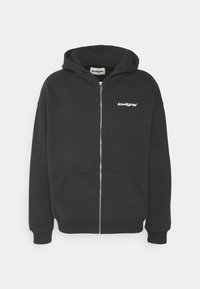 Sudadera con cremallera negra hecha de una mezcla de algodón. Cuenta con una capucha, bolsillos frontales y un pequeño logo blanco en la parte izquierda del pecho.