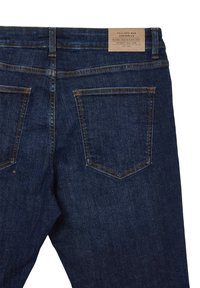 Jeans in denim blu scuro con una finitura testurizzata, dotati di due tasche posteriori, cuciture a contrasto e un'etichetta marrone in vita.