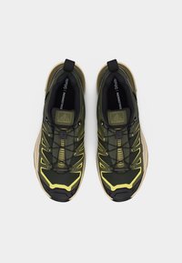 Ζεύγος παπουτσιών trail running Salomon σε ελαιώδη πράσινο και κίτρινο χρώμα με σύστημα γρήγορου δέσιμου κορδονιών και μπεζ σόλες, φαίνεται από πάνω σε λευκό φόντο.