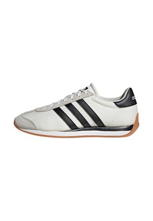Sneaker bianca con strisce nere, punta in suede grigio, suola in gomma e linguetta nera sul tallone con design a profilo basso.