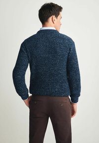 Granatowy sweter wełniany o rypsowym splocie i długich rękawach, z okrągłym dekoltem i elastycznymi mankietami, w połączeniu z brązowymi spodniami.