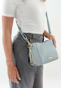 Bolso cruzado de cuero azul claro con herrajes dorados. Presenta una superficie texturizada, acentos de cadena y una correa ajustable.