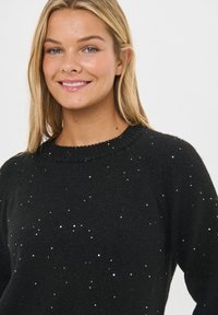 Czarny sweter wykonany z miękkiego materiału, z prążkowanym dekoltem i rozsianymi srebrnymi cekinami na teksturowanej powierzchni.